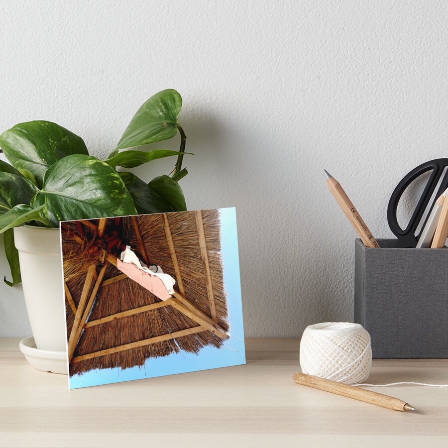 Straw beach umbrella, seen from below, two pink and white t-shirts hanging from it, cloudless blue sky Art Board Print