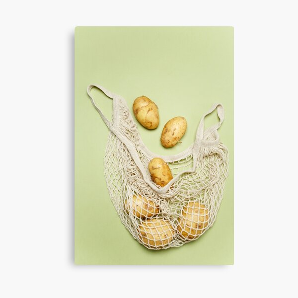 Trendy string bag with fresh young potatoes inside over light green background Canvas Print