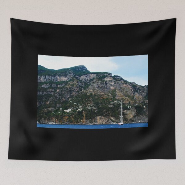 Item preview, View in Amalfi coast at a huge mountain with rocky parts, greenery and buildings with a white boat underneath designed and sold by Kristina Drozd.