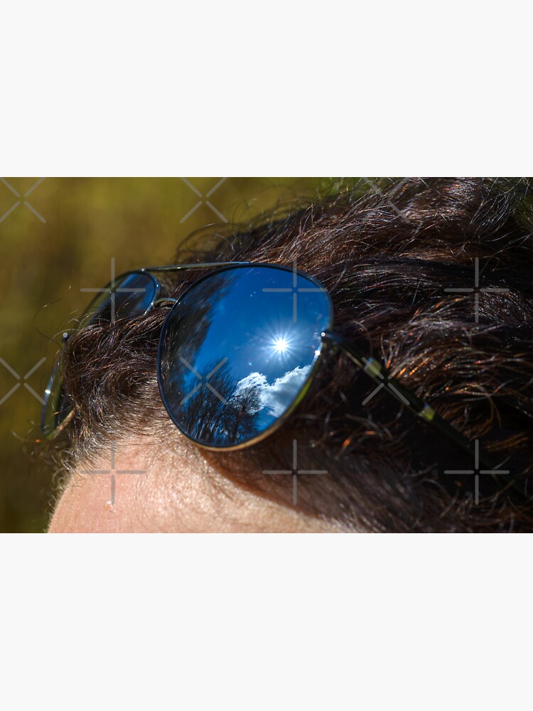 "Sunglasses, with reflection of blue cloudy sky and sun, on the woman's forehead" Sticker for