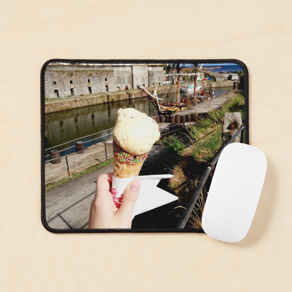 Person holding an ice cream cone near a sailboat and an old building, sunny day with clouds in the sky Mouse Pad