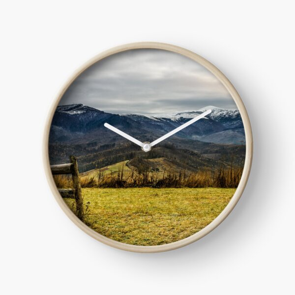 fence on the meadow in snowy mountains Clock