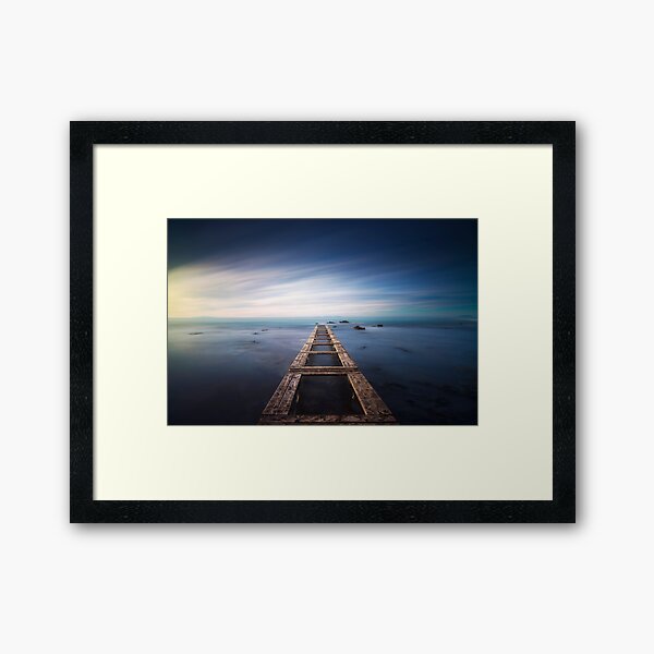 Wooden pier remains in a blue sea. Long Exposure. Framed Art Print