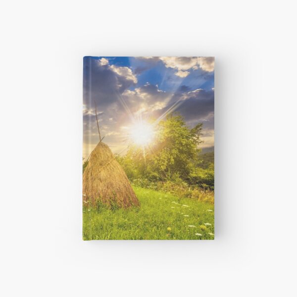 field with haystacks on hillside at sunset Hardcover Journal