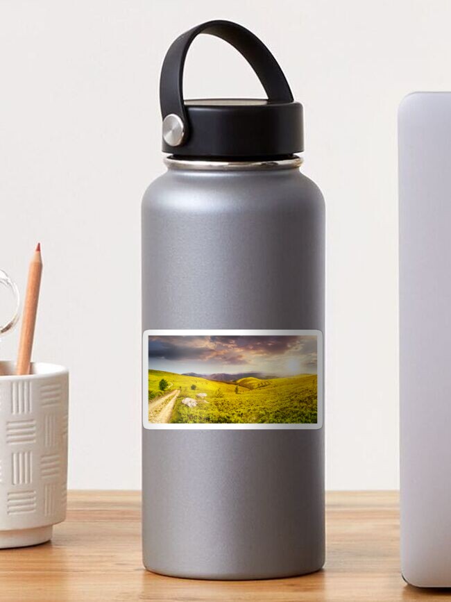 Thumbnail 1 of 3, Sticker, road on hillside meadow in mountain panorama at sunset designed and sold by mike-pellinni.
