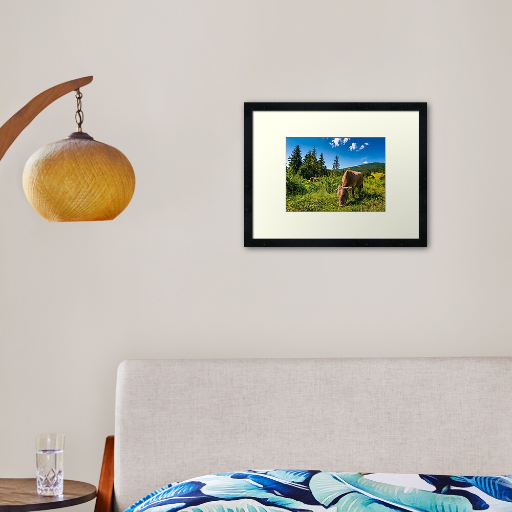 cow grazing in a tall grass near the forest Framed Art Print