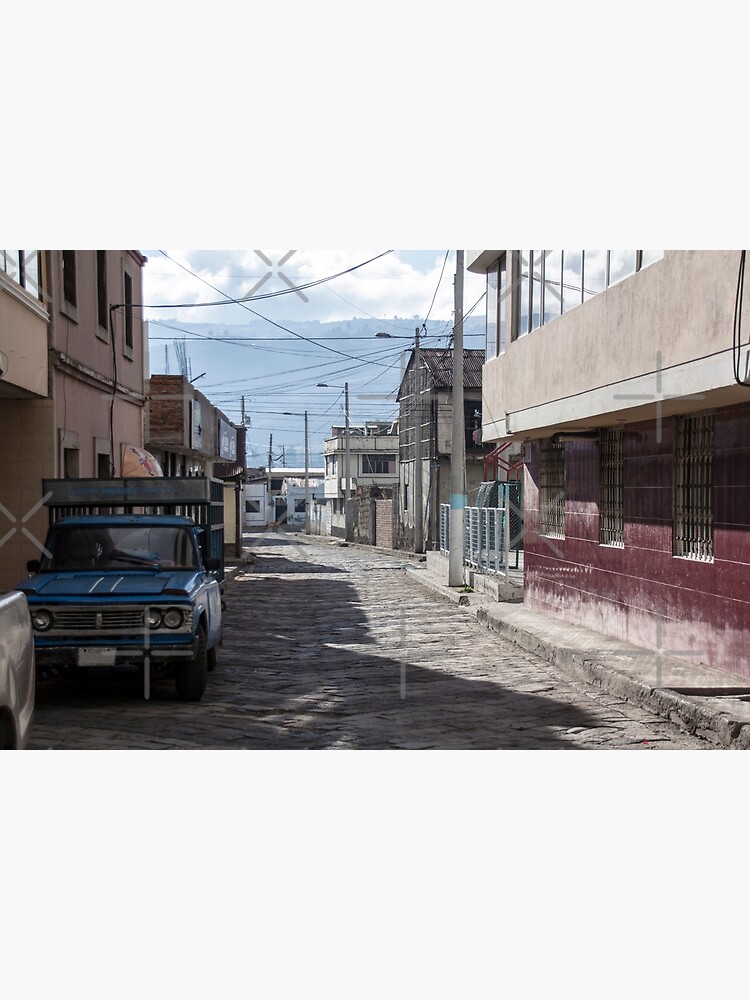 Empty quiet winding cobblestone street in Guamote, Ecuador with blue truck, red tile building, power lines and street lamps by kpander