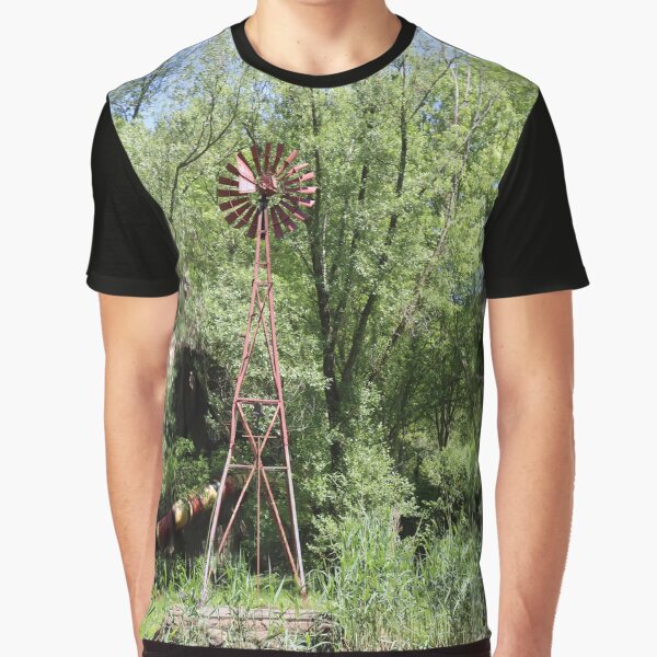 Item preview, Old fashioned metal windmill for natural energy conversion antique windmill near water and green forest behind designed and sold by Jacobs-Media.