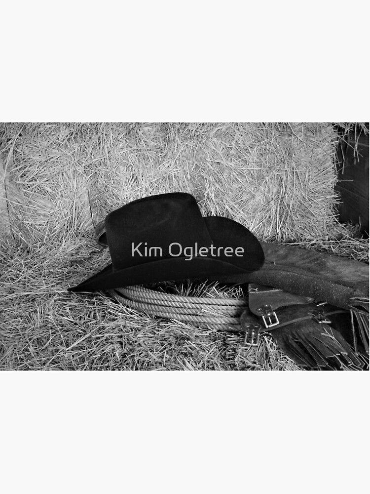 Black western style cowboy hat on a bale of hay with chaps and a