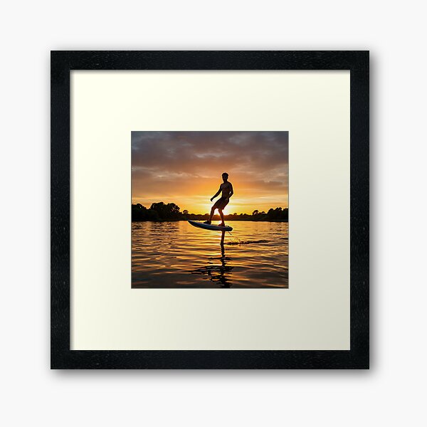 Item preview, Young adult male hydrofoiling on water at sunset, silhouetted against a vibrant orange and cloudy sky designed and sold by homydesign.