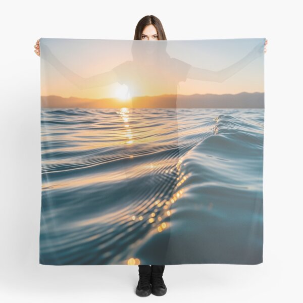 Item preview, Waves shimmer on the water's surface as the sun sets over distant mountains, creating a warm, golden glow designed and sold by homydesign.