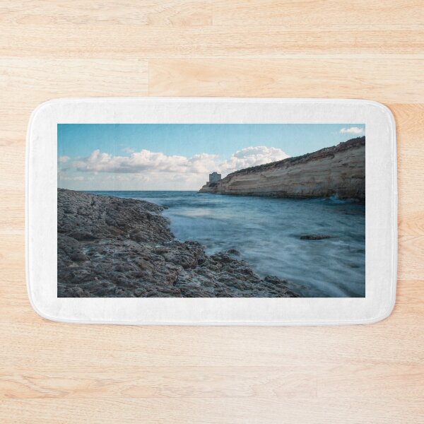 Item preview, Coastal Rocky Shoreline With Turquoise Water, Cliff, And Distant Tower Over Calm Sea designed and sold by Nmallia.