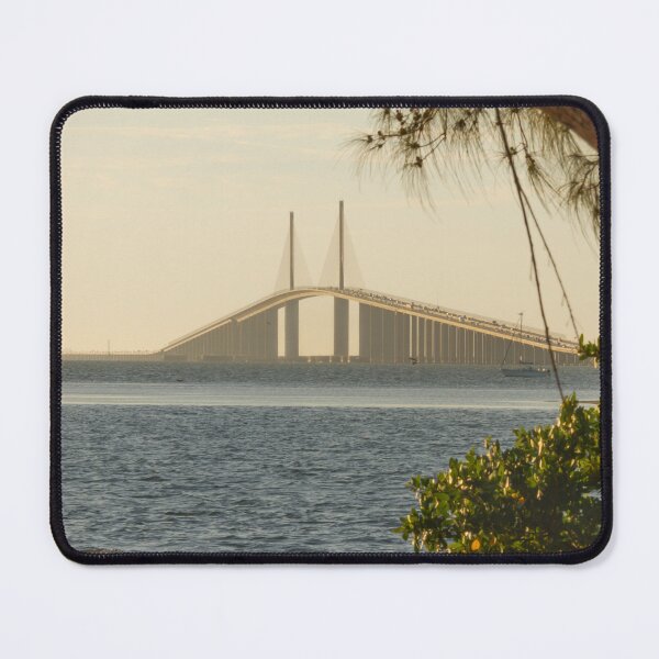 Item preview, A vibrant sunrise casts a golden glow over the Sunshine Skyway Bridge, perfectly framed by lush foliage designed and sold by EyezWatchin.