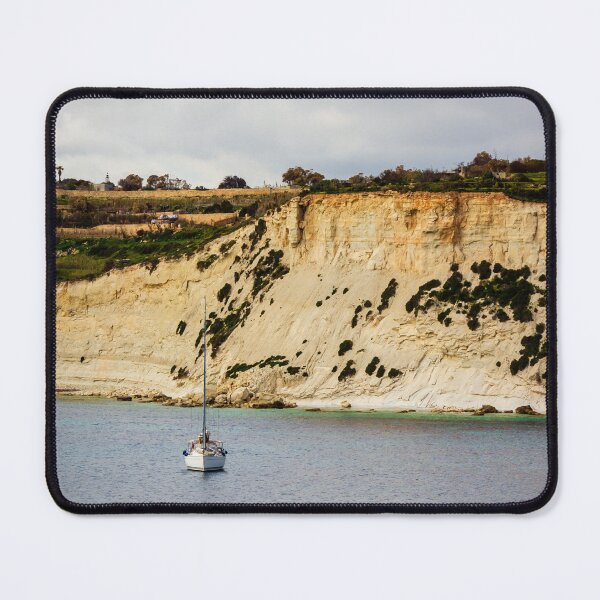 Item preview, Sailboat Anchored Below Dramatic Limestone Cliffs Along Quiet Coastal Bay Under Overcast Sky designed and sold by Nmallia.