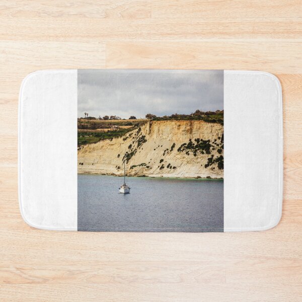 Item preview, Sailboat Anchored Below Dramatic Limestone Cliffs Along Quiet Coastal Bay Under Overcast Sky designed and sold by Nmallia.