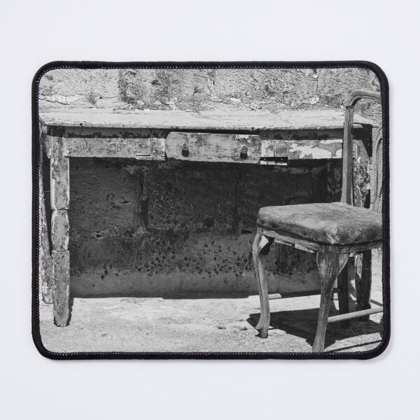 Item preview, Weathered Vintage Chair And Rustic Desk Against Textured Stone Wall In Monochrome Outdoor Scene designed and sold by Nmallia.