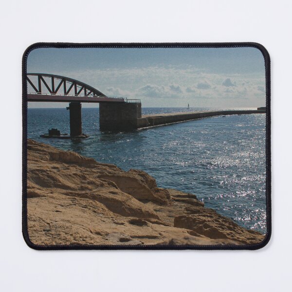 Item preview, Sunlit Rocky Coastline With Arched Bridge and Distant Lighthouse Over Sparkling Blue Sea designed and sold by Nmallia.