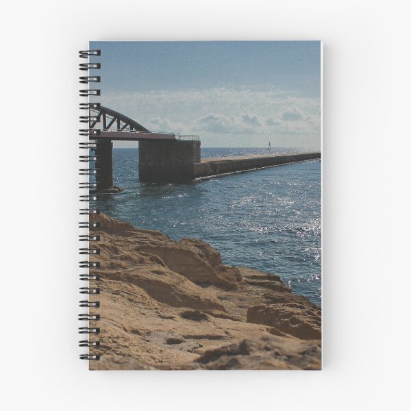 Item preview, Sunlit Rocky Coastline With Arched Bridge and Distant Lighthouse Over Sparkling Blue Sea designed and sold by Nmallia.