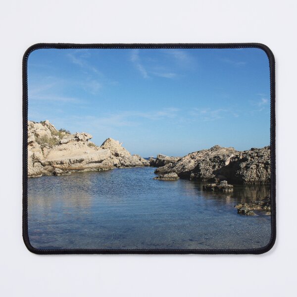 Item preview, Sunlit Rocky Coastline With Clear Blue Water and Calm Sea Under A Bright Sky designed and sold by Nmallia.