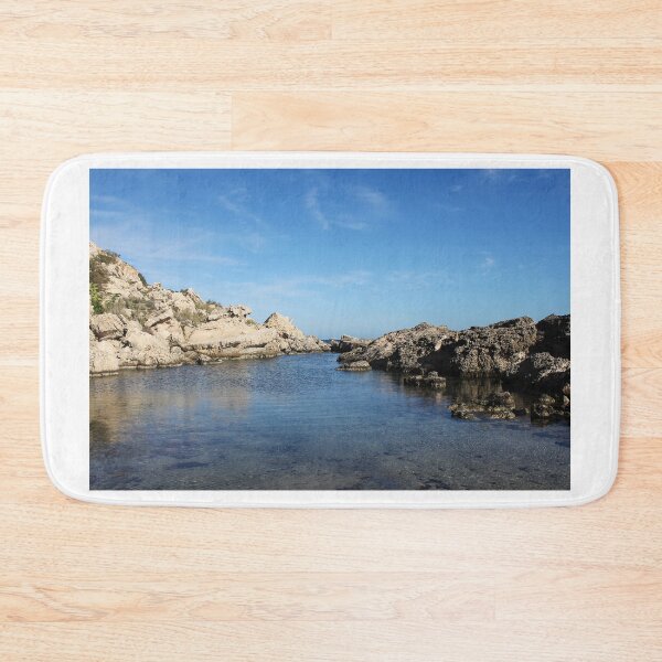 Item preview, Sunlit Rocky Coastline With Clear Blue Water and Calm Sea Under A Bright Sky designed and sold by Nmallia.