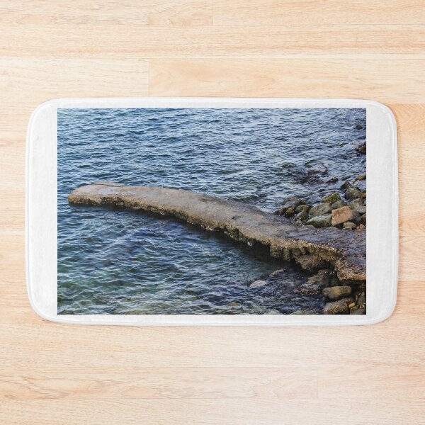 Item preview, Weathered Concrete Jetty Extending Over Rocky Shoreline Into Calm Blue Sea At Coast designed and sold by Nmallia.
