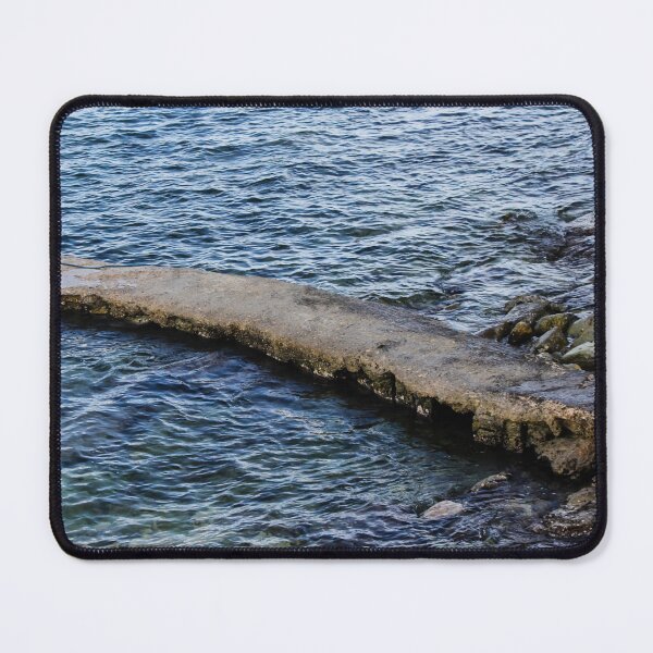 Item preview, Weathered Concrete Jetty Extending Over Rocky Shoreline Into Calm Blue Sea At Coast designed and sold by Nmallia.