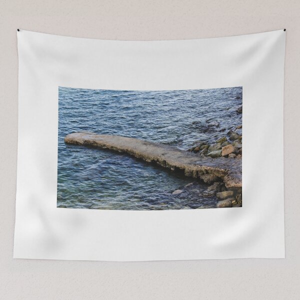 Item preview, Weathered Concrete Jetty Extending Over Rocky Shoreline Into Calm Blue Sea At Coast designed and sold by Nmallia.