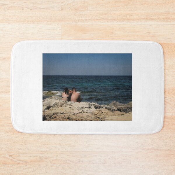 Item preview, Couple Sitting On Rocky Shoreline Looking Out At Blue Ocean Horizon On Summer Day designed and sold by Nmallia.