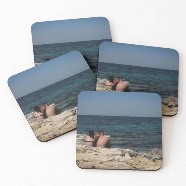 Item preview, Couple Sitting On Rocky Shoreline Looking Out At Blue Ocean Horizon On Summer Day designed and sold by Nmallia.