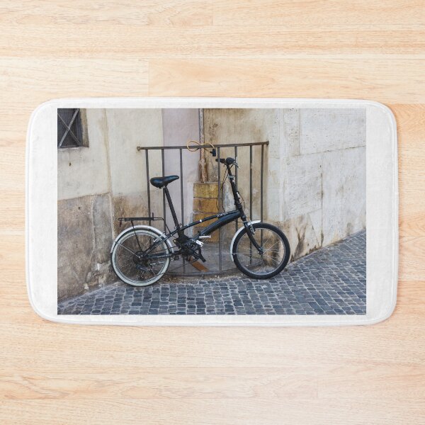 Item preview, Black Folding Bicycle Locked to Iron Rail on Cobblestone Street Beside Old Stone Wall designed and sold by Nmallia.