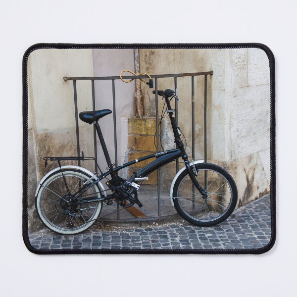 Item preview, Black Folding Bicycle Locked to Iron Rail on Cobblestone Street Beside Old Stone Wall designed and sold by Nmallia.