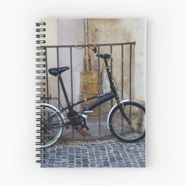 Item preview, Black Folding Bicycle Locked to Iron Rail on Cobblestone Street Beside Old Stone Wall designed and sold by Nmallia.