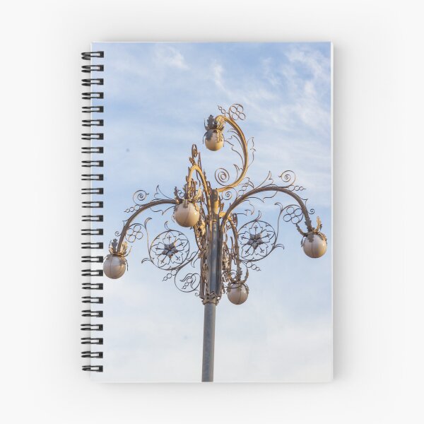 Item preview, Ornate Decorative Street Lamp With Floral Metalwork and Globe Lights Against Blue Sky designed and sold by Nmallia.