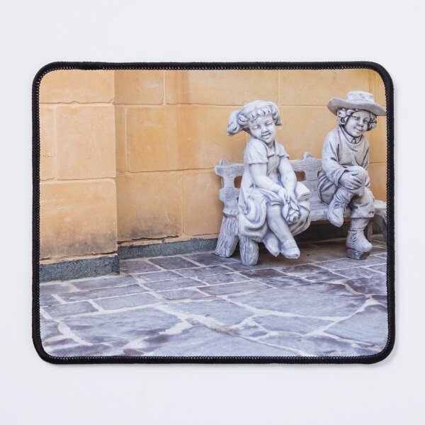 Item preview, Two Child Statues Sitting on a Bench Against a Rustic Wall in a Sunny Courtyard designed and sold by Nmallia.