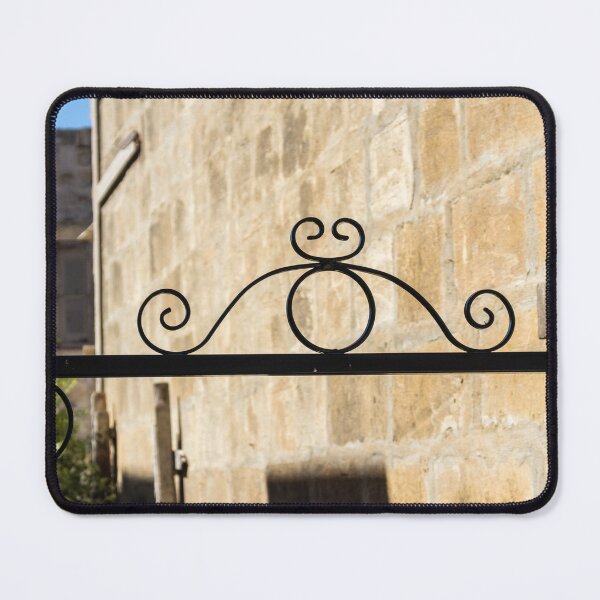 Item preview, Wrought Iron Decorative Gate Bracket With Scrollwork Against Sunlit Stone Wall in Historic Courtyard designed and sold by Nmallia.