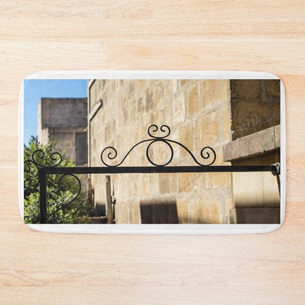 Item preview, Wrought Iron Decorative Gate Bracket With Scrollwork Against Sunlit Stone Wall in Historic Courtyard designed and sold by Nmallia.