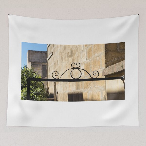 Item preview, Wrought Iron Decorative Gate Bracket With Scrollwork Against Sunlit Stone Wall in Historic Courtyard designed and sold by Nmallia.
