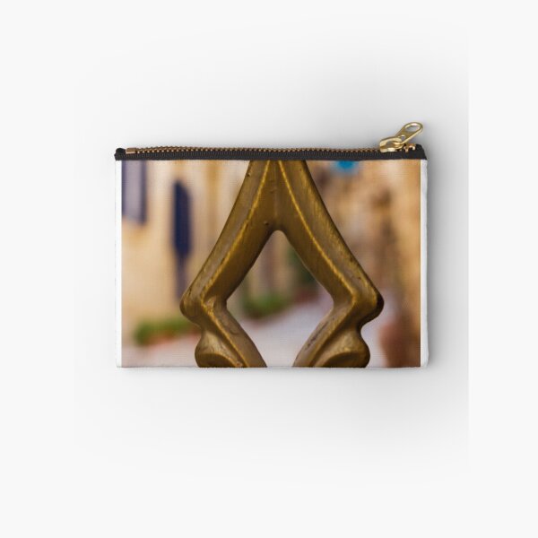 Artikelvorschau, Nahaufnahme einer Messing-Zierspitze an einem verzierten Zaun mit sanftem Straßenbokeh und warmen mediterranen Farbtönen entworfen und verkauft von Nmallia.
