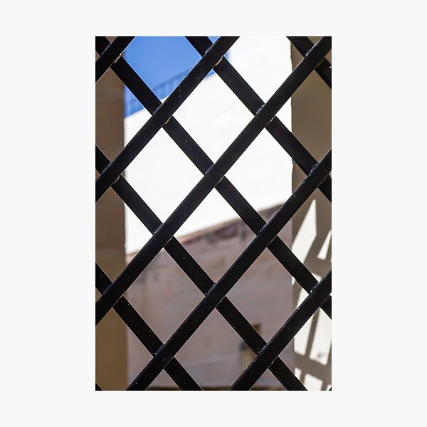 Item preview, Black Metal Lattice Fence With Diamond Pattern Framing Bright Urban Building And Blue Sky Background designed and sold by Nmallia.