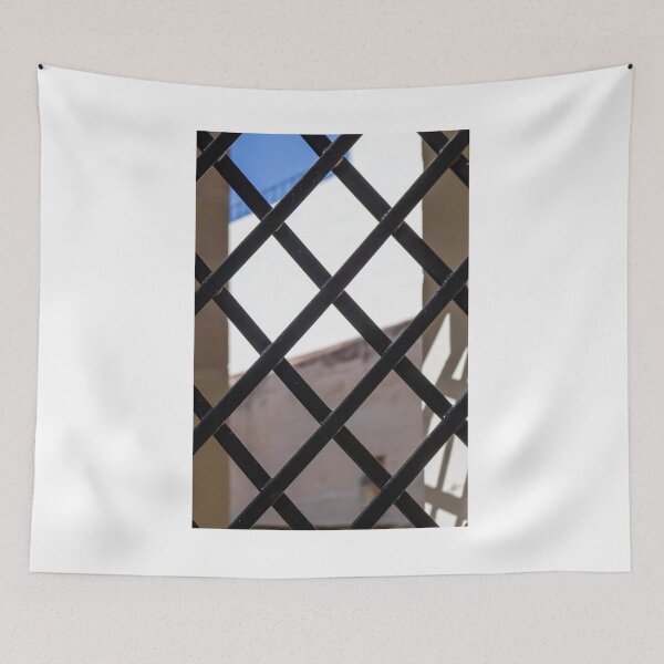 Item preview, Black Metal Lattice Fence With Diamond Pattern Framing Bright Urban Building And Blue Sky Background designed and sold by Nmallia.