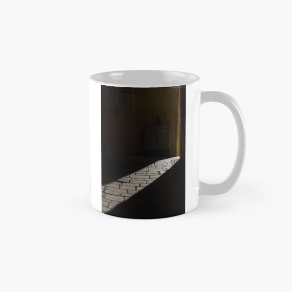 Item preview, Diagonal Sunlight on Cobblestone Alleyway Casting Dramatic Shadow in Narrow Urban Passage designed and sold by Nmallia.