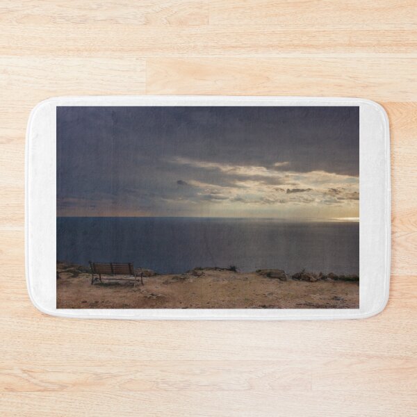 Item preview, Solitary Bench Overlooking Calm Ocean Horizon Under Dramatic Sunset Clouds On Rocky Cliff designed and sold by Nmallia.