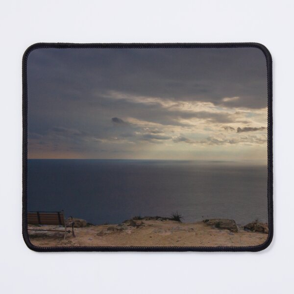 Item preview, Solitary Bench Overlooking Calm Ocean Horizon Under Dramatic Sunset Clouds On Rocky Cliff designed and sold by Nmallia.