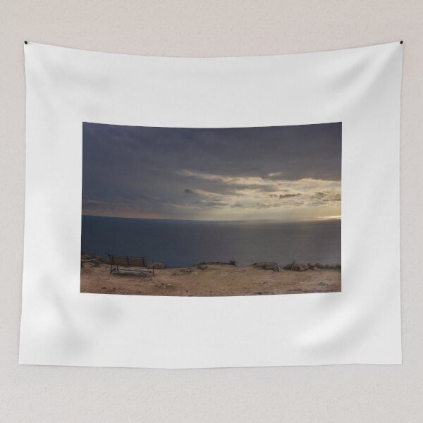 Item preview, Solitary Bench Overlooking Calm Ocean Horizon Under Dramatic Sunset Clouds On Rocky Cliff designed and sold by Nmallia.