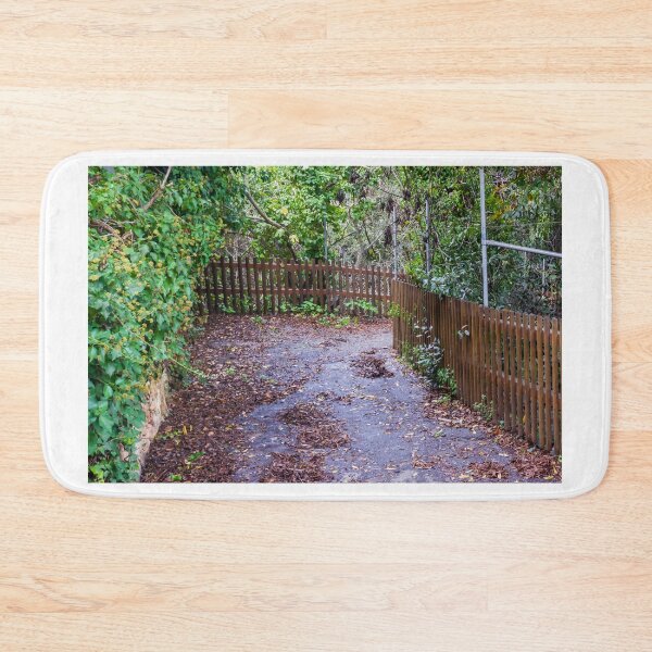 Item preview, Leaf-Covered Garden Path With Wooden Fence Curving Through Lush Greenery In Autumn designed and sold by Nmallia.