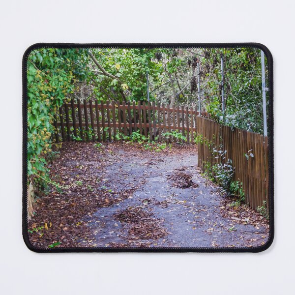 Item preview, Leaf-Covered Garden Path With Wooden Fence Curving Through Lush Greenery In Autumn designed and sold by Nmallia.