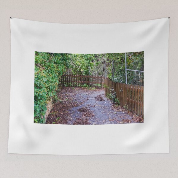 Item preview, Leaf-Covered Garden Path With Wooden Fence Curving Through Lush Greenery In Autumn designed and sold by Nmallia.
