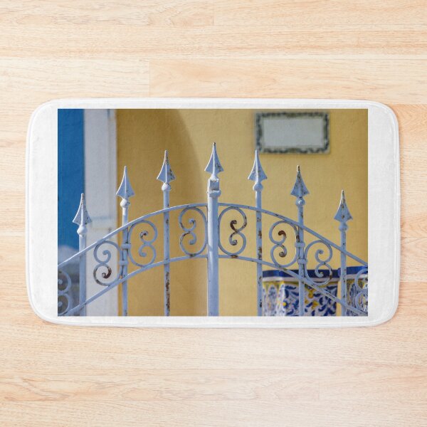 Item preview, Sunlit Ornate Wrought Iron Gate With Rust Patina Against Yellow Wall and Blue Ceramic Planter designed and sold by Nmallia.