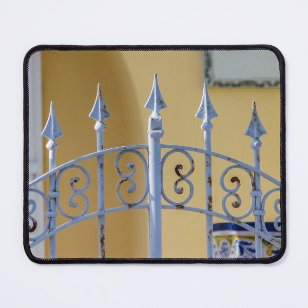 Item preview, Sunlit Ornate Wrought Iron Gate With Rust Patina Against Yellow Wall and Blue Ceramic Planter designed and sold by Nmallia.