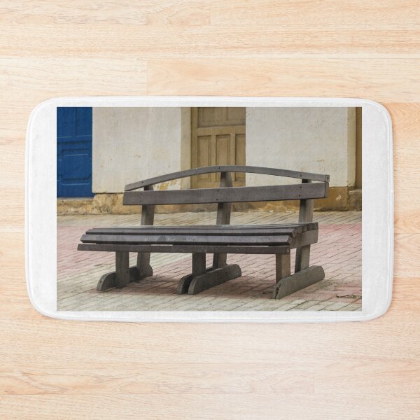 Item preview, Empty Wooden Bench on Quiet Street Pavement Near Old Doorway in Rustic Urban Courtyard designed and sold by Nmallia.